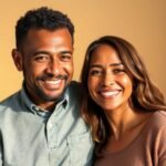 A multiracial couple smiles brightly, sitting close together against a warm-toned background.